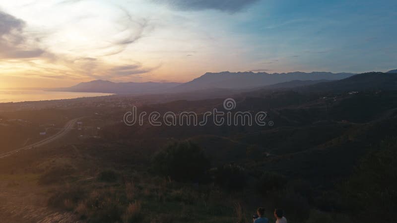 Eine dreiköpfige Familie, die auf einem Hügel steht und den malerischen Sonnenuntergang über einer weitläufigen Landschaft mit ein stock footage