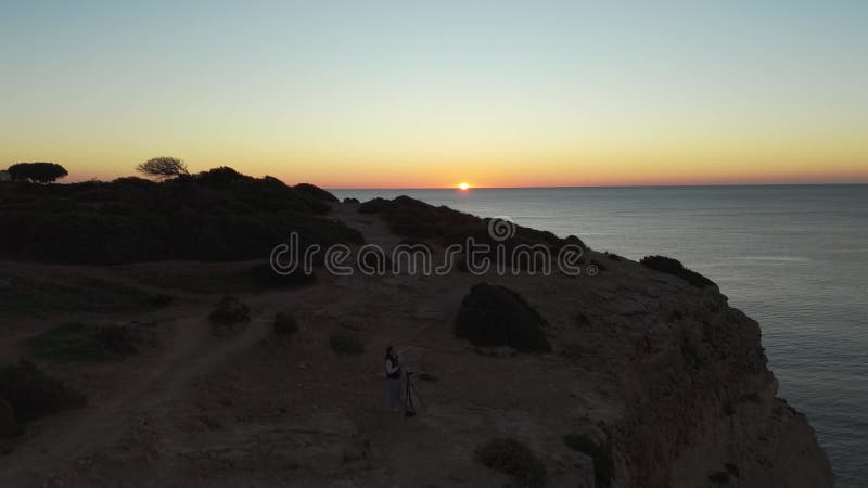 Eine Einzelfrau, die ihr Stativ auf zerklüfteten Algarve-Felsen in der Nähe von carvoeiro portugal aufbaut, um das stock video