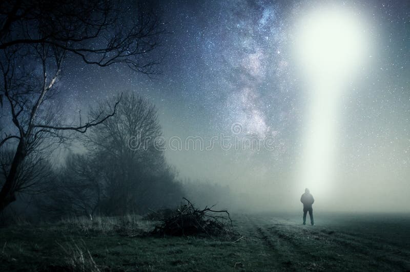 A concept of a UFO above a lone hooded figure with a light beam coming down. Standing on a path on a spooky misty night, with a cold grainy blue edit. A concept of a UFO above a lone hooded figure with a light beam coming down. Standing on a path on a spooky misty night, with a cold grainy blue edit.
