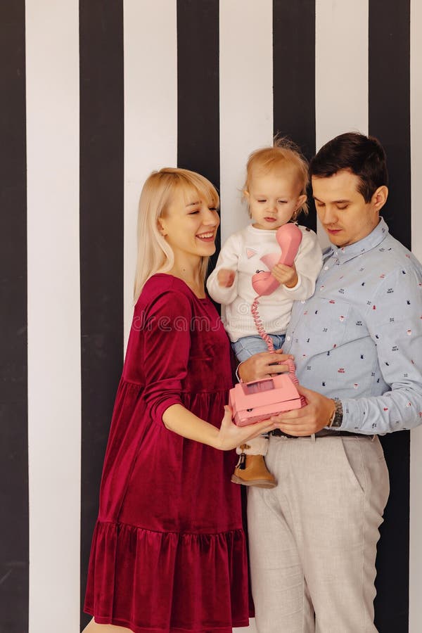 Eine Familie mit einer kleinen Tochter, die durch rosafarbenes Retro- Telefon, einen einfachen Hintergrund, Glück und Freude spri stockbild Eine Familie mit einer kleinen Tochter, die durch rosafarbenes Retro- Telefon, einen einfachen Hintergrund, Glück und Freude spri stockbild