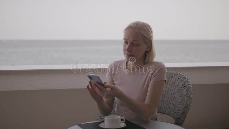 Eine Frau benutzt ein Smartphone auf dem Balkon ihres Hotelzimmers mit Meerblick..