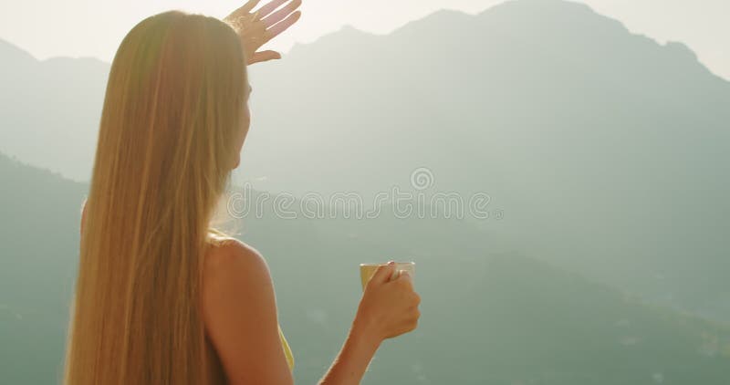 Eine Frau blockiert die Sonne, während sie eine Teetasse mit der Hand hält. Goldene Stunde Licht umhüllt Weibchen gegen bergige Um