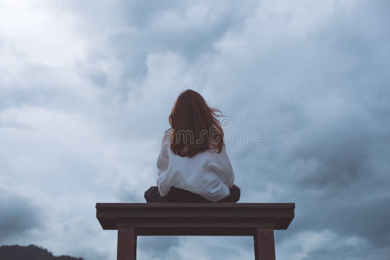 Eine Frau, die allein auf einer Holzbank im Park mit bewölktem und düsterem Himmel sitzt lizenzfreie stockfotos