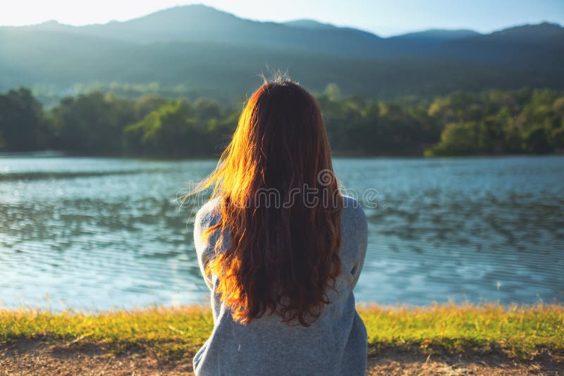 Eine Frau, die allein am See sitzt und die Berge mit grüner Natur betrachtet lizenzfreie stockbilder