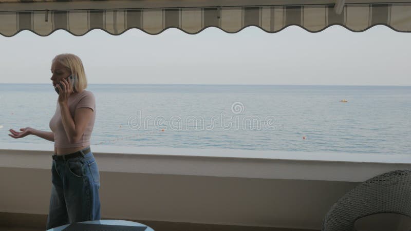 Eine Frau, die auf dem Balkon eines Hotelzimmers mit Meerblick telefoniert.