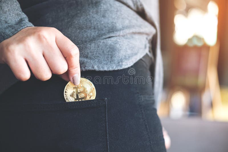 Closeup image of a woman picking up and dropping bitcoin into a black jean pocket. Closeup image of a woman picking up and dropping bitcoin into a black jean pocket