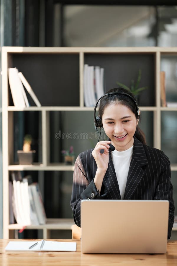 Eine Frau, die ein Headset trägt, lächelt, während sie an einem Laptop arbeitet lizenzfreie stockfotografie