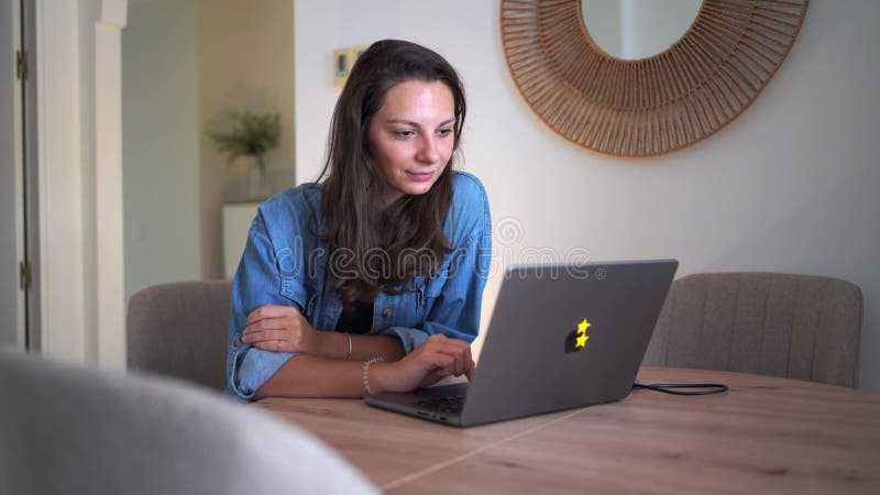 Eine Frau in einem blauen Denim-Shirt lächelnd während sie auf ihrem Laptop zu Hause genüsslich ihre Arbeit. stock video