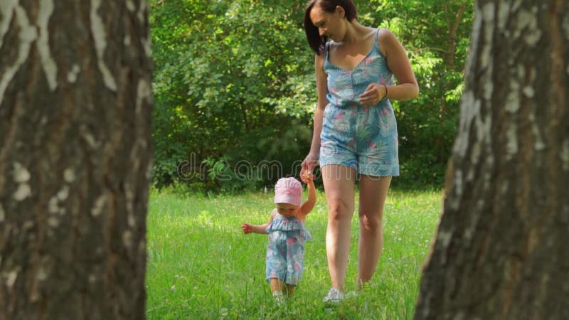 Eine Frau führt ein Baby durch die Hand auf dem Gras