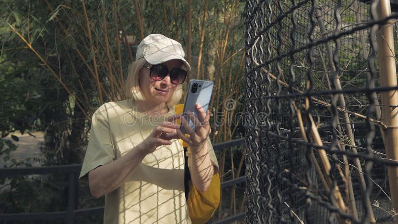 Eine Frau im Zoo, die neben dem Käfig steht, verwendet eine Smartphone-Kamera.