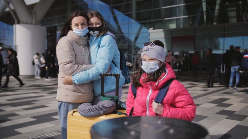 Eine Frau mit zwei Töchtern außerhalb des Gebäudes vor dem Flughafen-Terminal mit Koffern und medizinischem Tragen