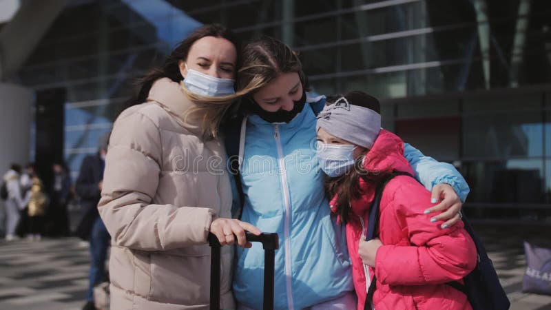 Eine Frau mit zwei Töchtern außerhalb des Gebäudes vor dem Flughafen-Terminal mit Koffern und medizinischem Tragen