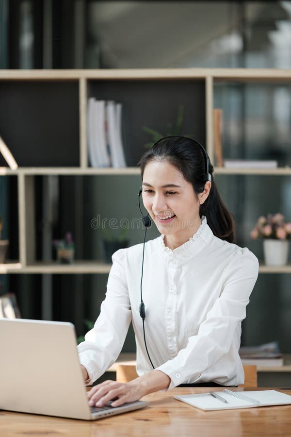 Eine Frau sitzt an einem Schreibtisch mit einem Laptop und einem Headset auf stockbild