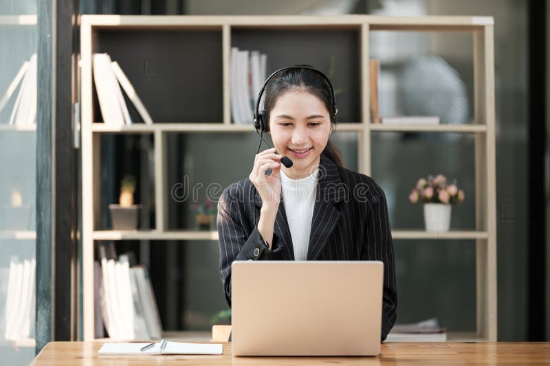 Eine Frau sitzt an einem Schreibtisch mit Laptop und Headset lizenzfreie stockbilder