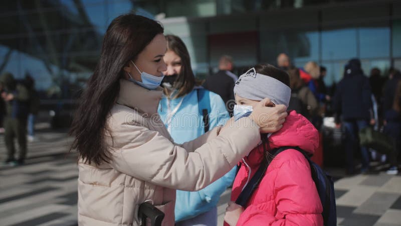 Eine Frau stellt ihre kleine Tochter mit einer medizinischen Maske auf, bevor sie das Flughafengebäude betritt.