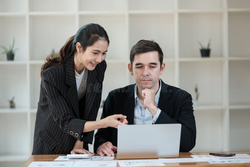 Eine Frau und ein Mann sitzen an einem Schreibtisch und schauen auf einen Laptop lizenzfreie stockfotos