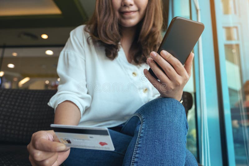 Eine Frauenholdingkreditkarte und Anwendung des beweglichen Bankwesens beim Sitzen im Café lizenzfreie stockfotografie Eine Frauenholdingkreditkarte und Anwendung des beweglichen Bankwesens beim Sitzen im Café lizenzfreie stockfotografie