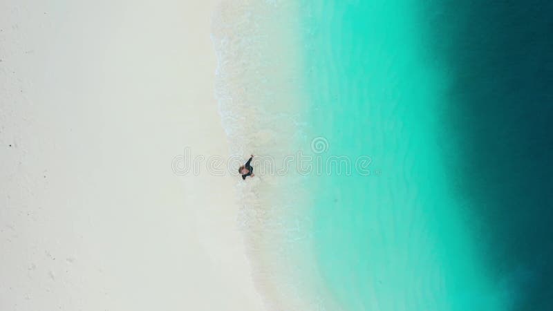 Eine glückliche Frau, die sich am weißen Sandstrand mit türkisfarbenem Ozean dreht. Oberansicht. stock footage