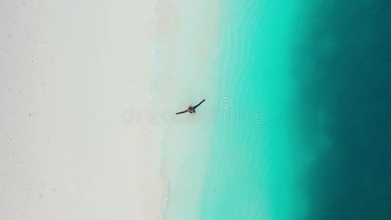 Eine glückliche Frau, die sich am weißen Sandstrand mit türkisfarbenem Ozean dreht. Oberansicht. stock footage