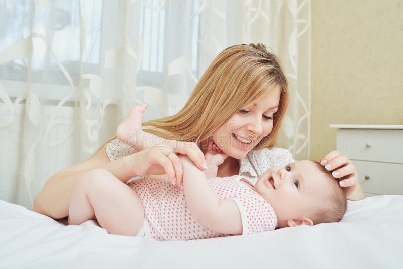 Eine glückliche Mutter mit einem Baby spielt auf einem Bett stockfotografie Eine glückliche Mutter mit einem Baby spielt auf einem Bett stockfotografie