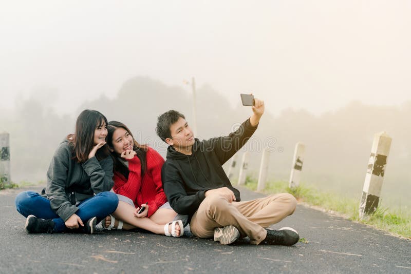 Eine Gruppe von drei asiatischen Freunden, die eine Strickjacke unter Verwendung eines selfie Telefons tragen, um Fotos in einer stockfotografie Eine Gruppe von drei asiatischen Freunden, die eine Strickjacke unter Verwendung eines selfie Telefons tragen, um Fotos in einer stockfotografie