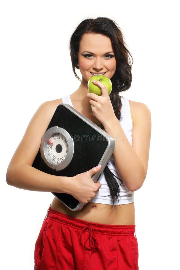 A young and brunette woman in red shorts with scales and a fresh green apple. The image is isolated on a white background. A young and brunette woman in red shorts with scales and a fresh green apple. The image is isolated on a white background.