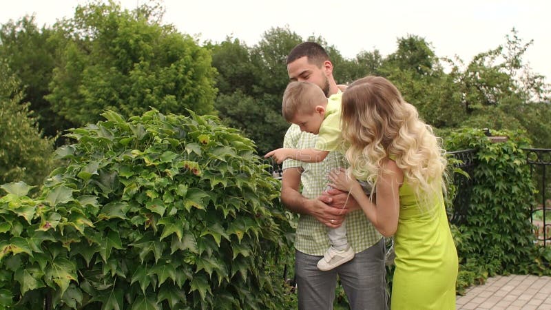 Eine junge Familie geht in einen Park unter grünen Büschen