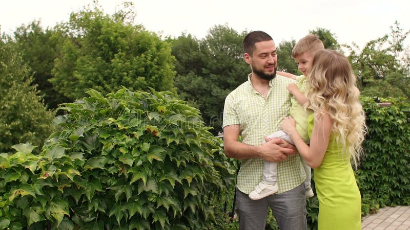 Eine junge Familie geht in einen Park unter grünen Büschen und Bäumen