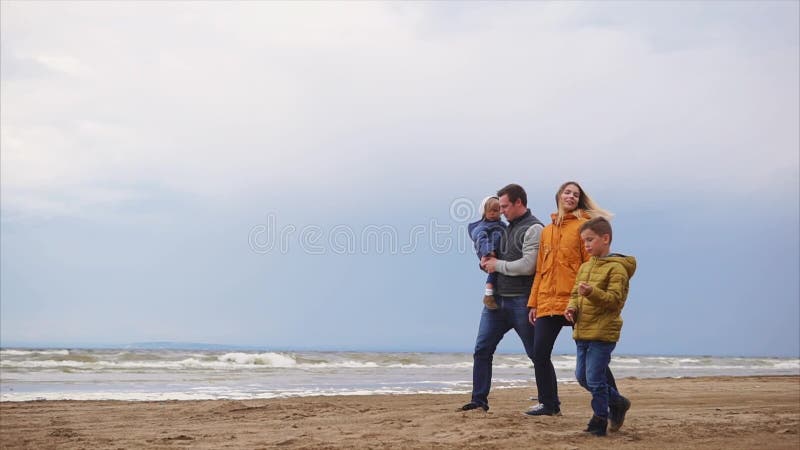 Eine junge Familie geht entlang den Strand im kühlen Wetter mit einem Drachen
