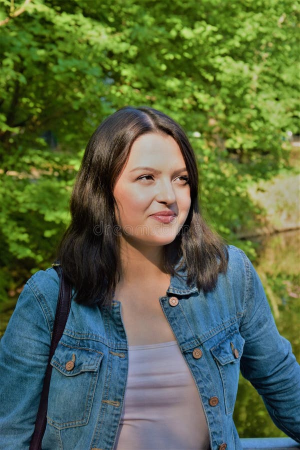 Eine junge Frau in einer Denimjacke steht im Park und schaut zur Seite lizenzfreie stockfotografie Eine junge Frau in einer Denimjacke steht im Park und schaut zur Seite lizenzfreie stockfotografie