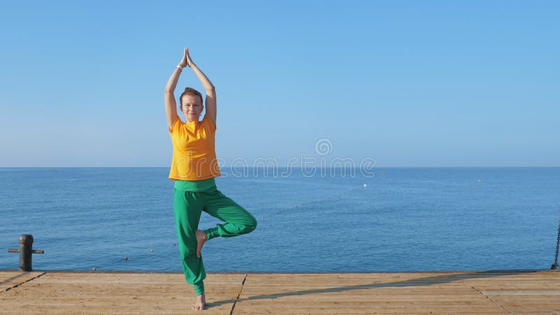 Eine junge Frau im bunten Kleidungspraxisyoga durch das Meer oder den Ozean.