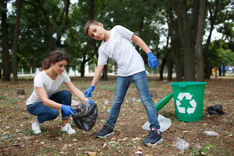 A full-length portrait of a child and a young women in blue latex gloves. A family picking up the plastic trash and putting it in a black garbage bag on a blurred park background. Pollution concept. A full-length portrait of a child and a young women in blue latex gloves. A family picking up the plastic trash and putting it in a black garbage bag on a blurred park background. Pollution concept.