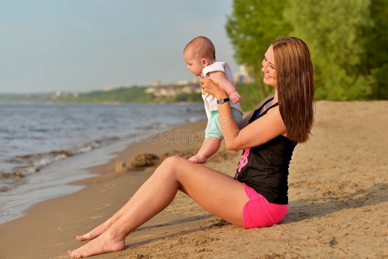 Eine junge Mutter mit einer kleinen Tochter sitzt auf einem sandigen Strand stockfotografie Eine junge Mutter mit einer kleinen Tochter sitzt auf einem sandigen Strand stockfotografie