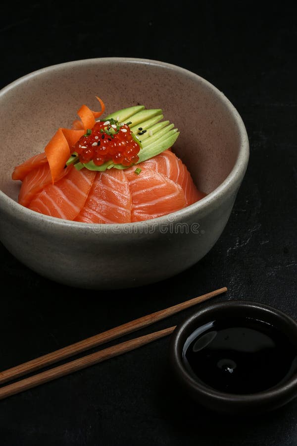 Eine Keramikschüssel gefüllt mit frischen Lachs Sashimi Avocado Scheiben und Ikura mit Sesamsamen Küken und Karottencurl stockbild