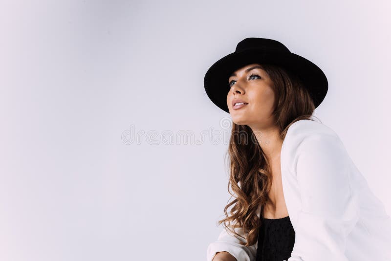 Eine lachende und Lächeln kastanienbraune behaarte Frau in einem weißen Kleid und in einem schwarzen Hut.. sittion auf der hölzern lizenzfreies stockbild
