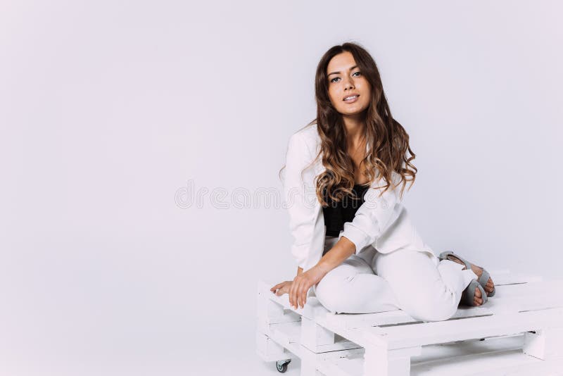Eine lachende und Lächeln kastanienbraune behaarte Frau in einem weißen Kleid und in einem schwarzen Hut.. sittion auf der hölzern stockfoto