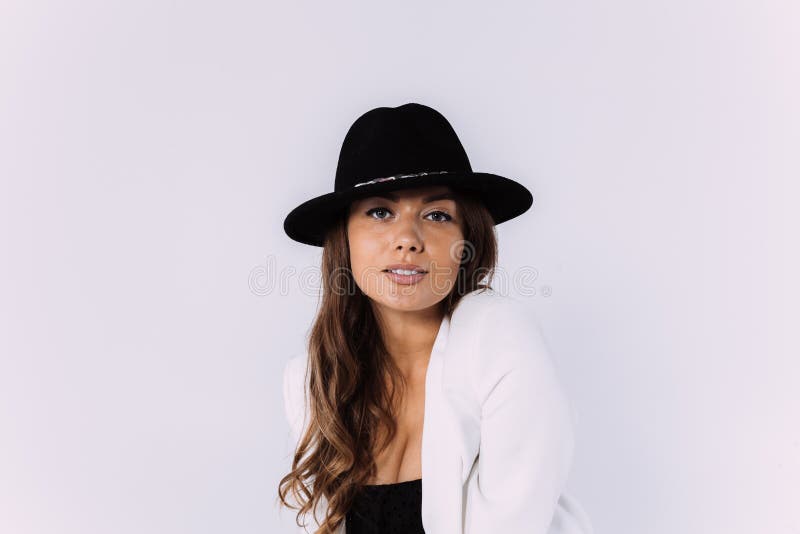 Eine lachende und Lächeln kastanienbraune behaarte Frau in einem weißen Kleid und in einem schwarzen Hut.. sittion auf der hölzern lizenzfreie stockfotos