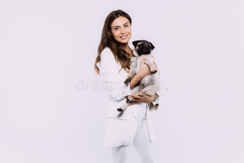 Eine lachende und Lächeln kastanienbraune behaarte Frau in einem weißen Kleid starrte mich am liebevollsten entlang ihrer freundlichen Pug an, der friedlich auf den Händen sitzt, die ihre ganze Aufmerksamkeit gewinnen. ein Einzelfall weißen Hintergrund