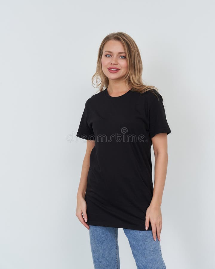 Eine lächelnde Frau mit langen Haaren mit schwarzem Hemd und blauen Jeans steht vor einem einfachen Hintergrund. Sie posiert mit b stockbilder