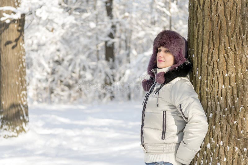 Eine lächelnde Frau steht im Wald, der einen Pelzhut trägt und stockfotografie