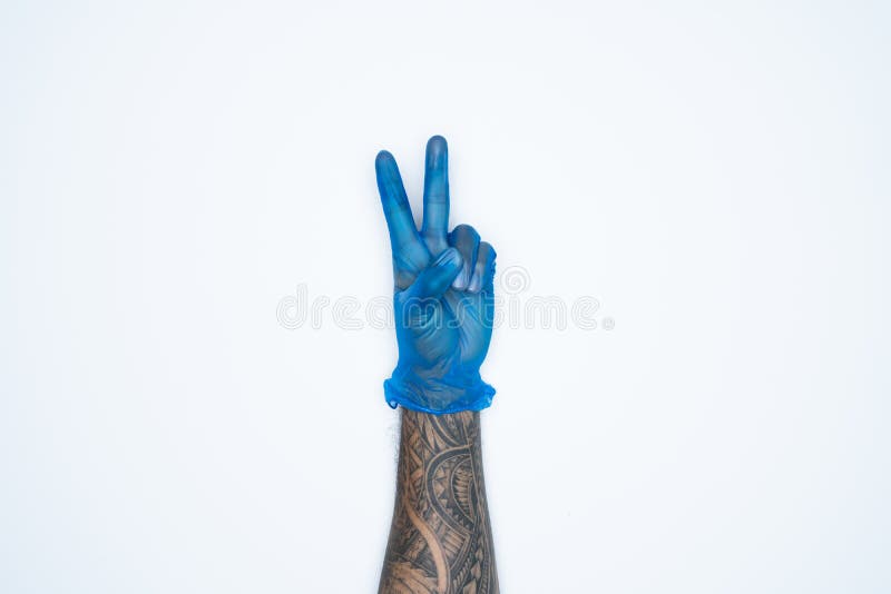 Eine Mannhand und -gesten im blauen Gummihandschuh zeigt das Zeichen mit zwei Fingern, das auf weißem Hintergrund befindet stockfotos