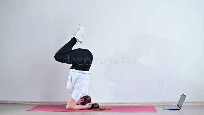 Eine mollige junge Frau sieht sich eine Online-Yogastunde auf einem Laptop an. Fernsport. Unterarmständer