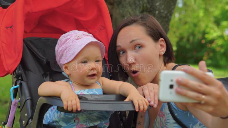 Eine Mutter macht selfie an einem Handy mit einem Baby in einem Spaziergänger