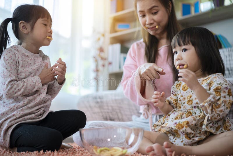Eine Mutter mit zwei Kindern, die im Wohnzimmer sitzen und Snacks essen. eine Mutter mit zwei jungen Töchtern hat zu Hause gefrühs stockfotografie