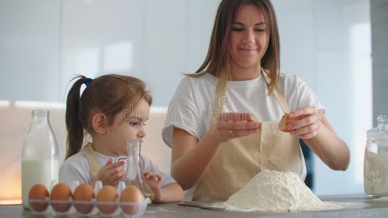 Eine Mutter und Tochter in den Schutzblechen brechen ein Ei und werfen es in das Mehl, um den Teig zu machen. stock footage