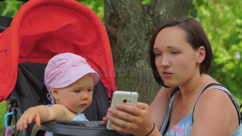 Eine Mutter zeigt einem Kind einen Handy in einem Spaziergänger