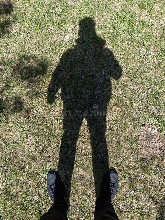 Eine Person, die mit ihrem Schatten auf dem Boden im Gras steht stockfoto