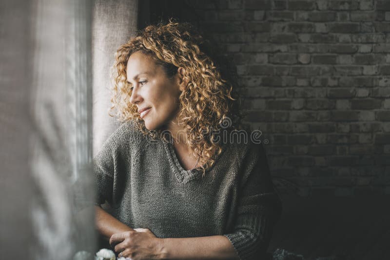 Eine ruhige erwachsene Frau, die nach Hause schaut, mit friedlichem Gesichtsausdruck und wenig Lächeln. selbstbewusste Frau stockfoto
