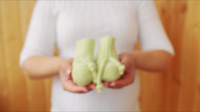 Eine schwangere Mutter in einem weißen T-Shirt erstreckt sich ihre Hand mit den Schuhen der kleine Kinder aus. Mama erstreckt sich
