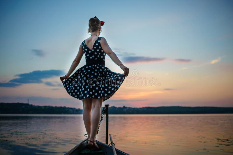 Eine schöne junge Frau kleidete das Bereitstehen des Sees, auf dem Hintergrund des Sonnenuntergangs lizenzfreie stockfotos Eine schöne junge Frau kleidete das Bereitstehen des Sees, auf dem Hintergrund des Sonnenuntergangs lizenzfreie stockfotos